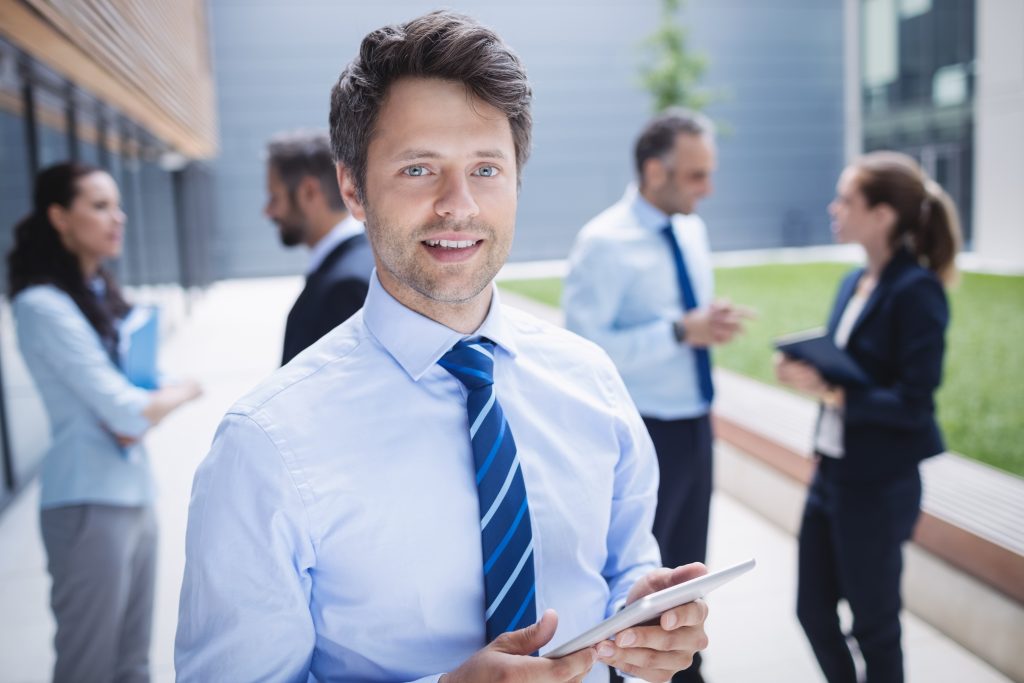 Portrait of a confident businessman holding digital tablet outside office building